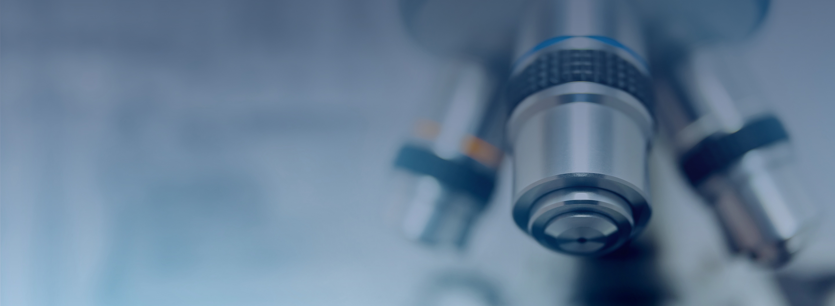 Close-up of microscope objective lenses in a lab, with a cool blue tone and shallow depth of field.