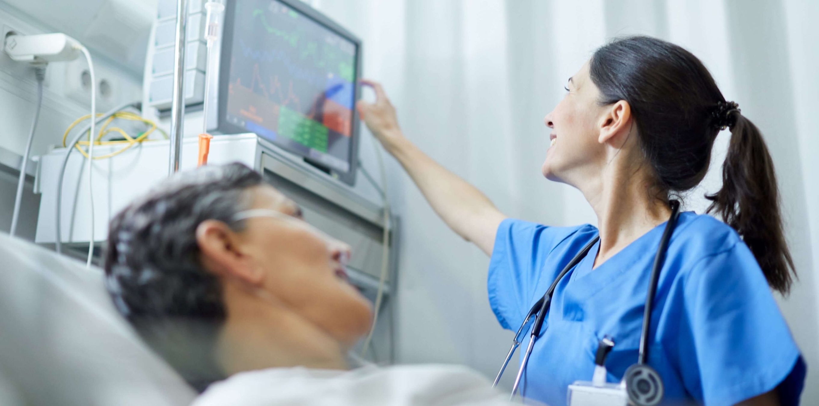 Nurse in scrubs checking a patient’s vital signs on a bedside monitor.