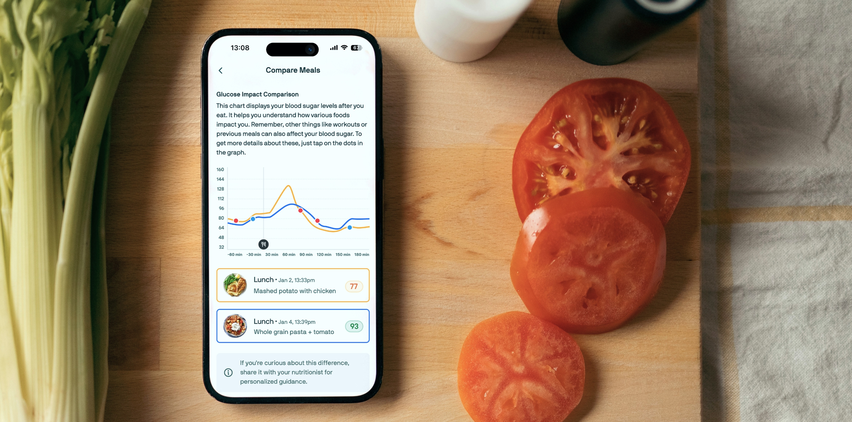 Smartphone showing a glucose-tracking app on a cutting board beside sliced tomatoes.