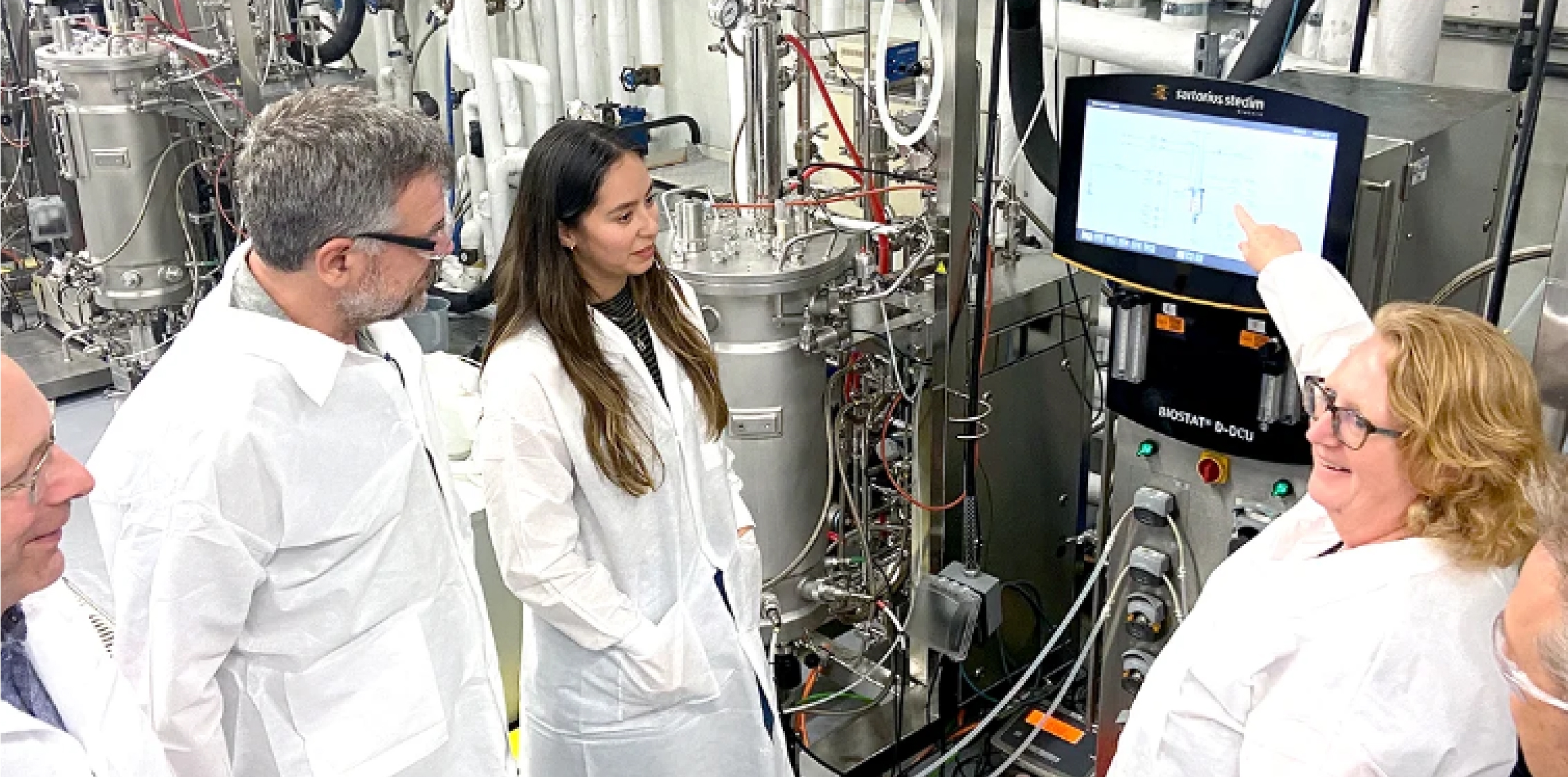 Team in lab coats reviewing data on a bioreactor control screen.