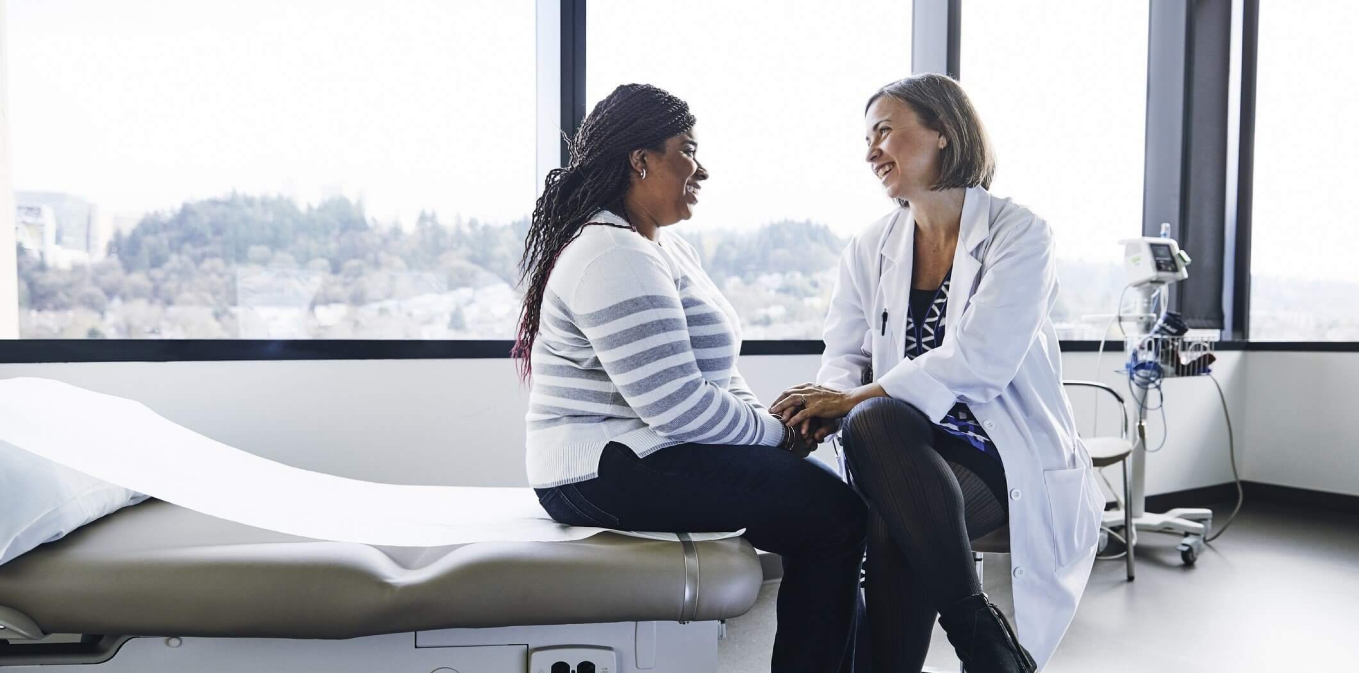 Clinician and patient smiling and holding hands during a consultation in a clinic exam room.