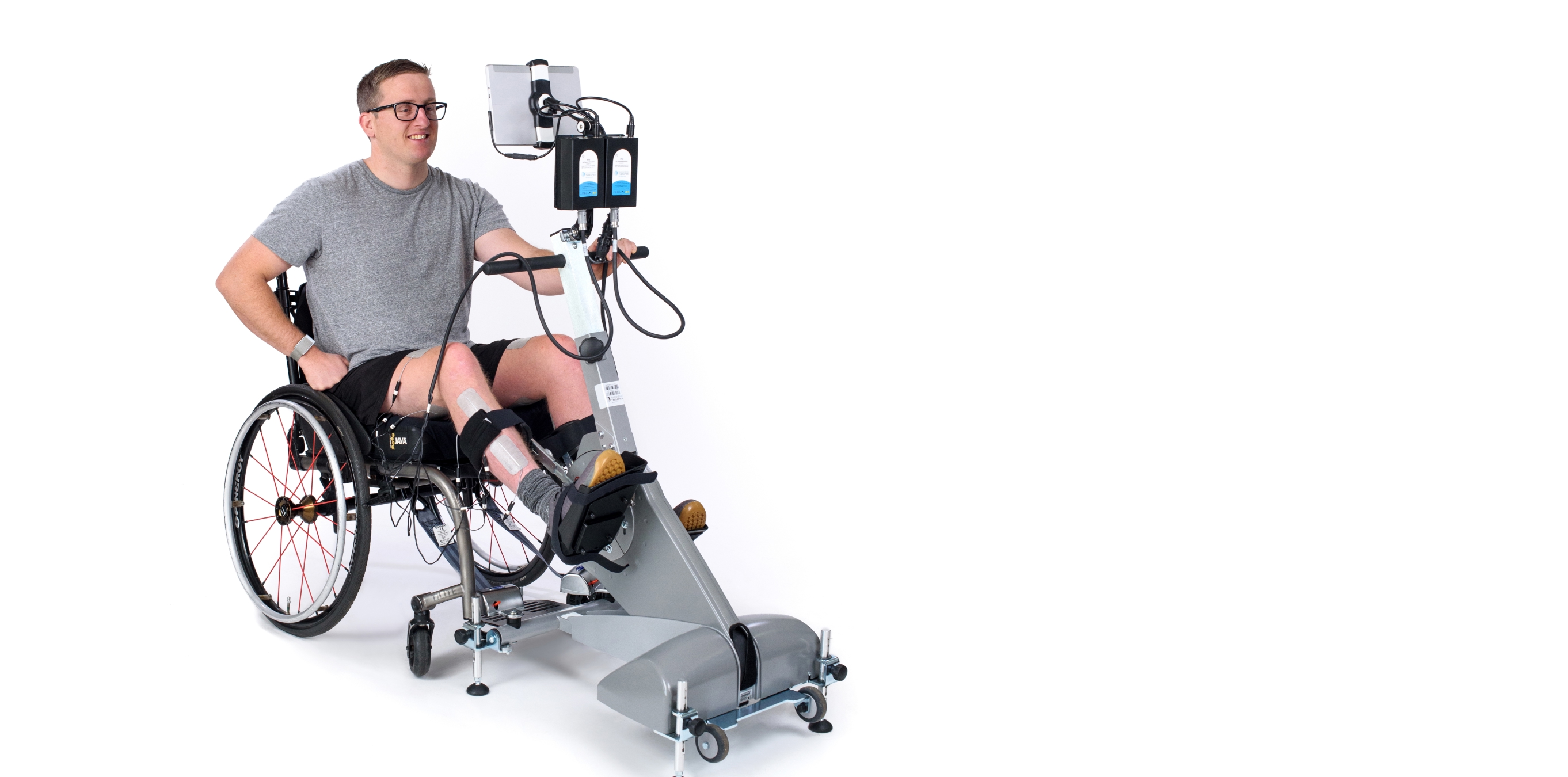 Wheelchair user pedaling a rehabilitation FES cycling device on a white background.