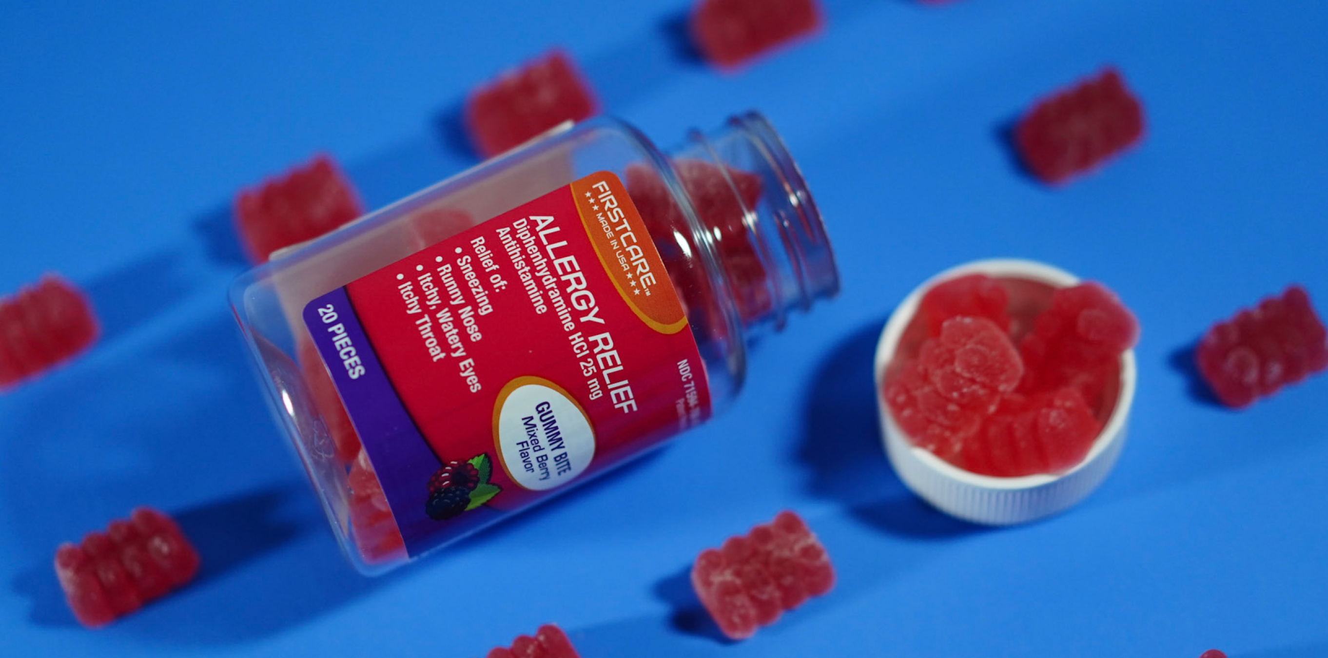 Allergy relief gummy bottle tipped over with red bear-shaped gummies on a blue background.