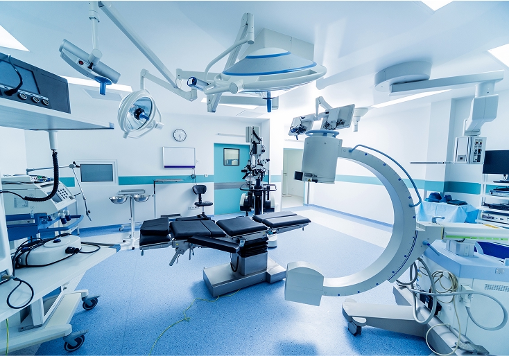 Modern operating room with surgical table, overhead lights, and a C-arm imaging system.