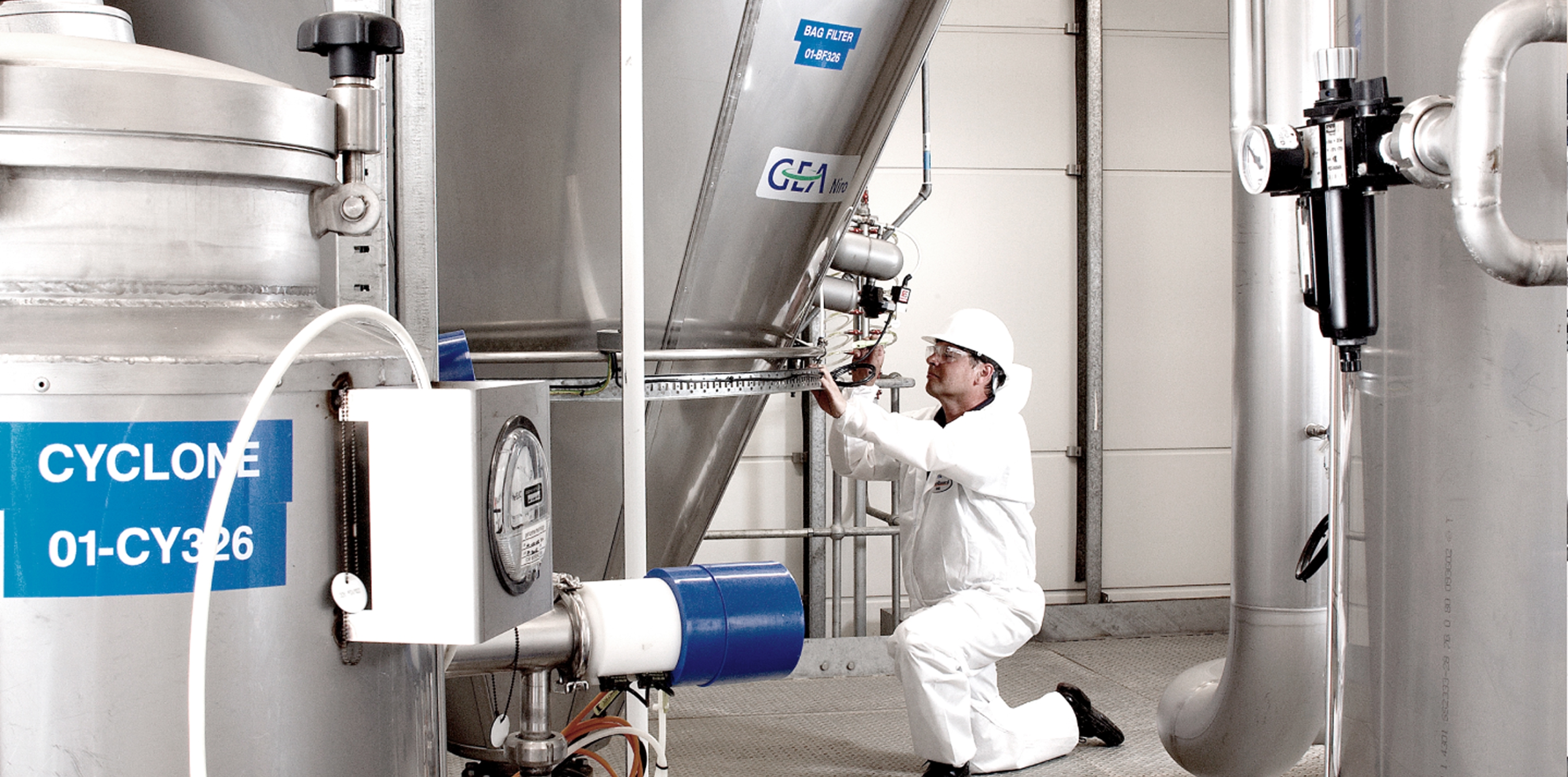 Worker in white PPE adjusts stainless-steel processing equipment in a plant.