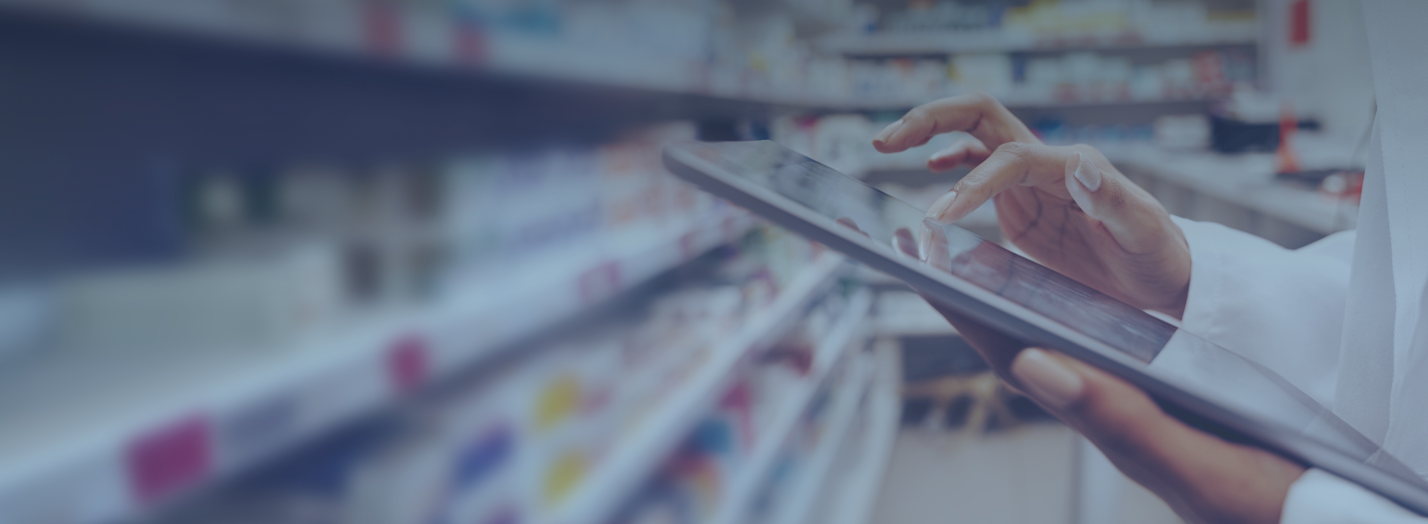 Pharmacist reviewing inventory on a tablet in a pharmacy aisle.